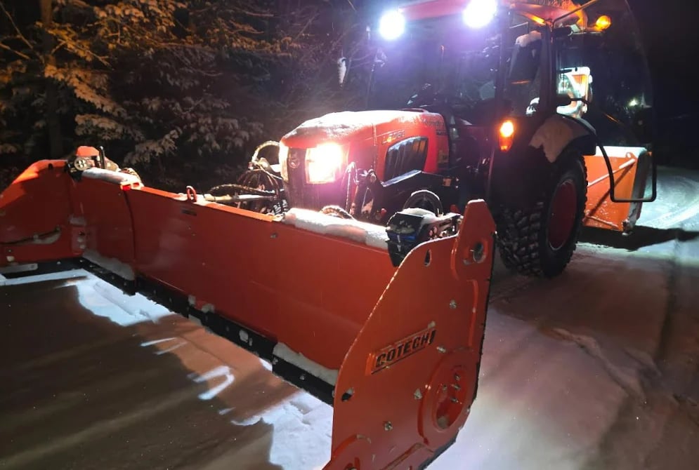Red snow plow truck with blade attachment clearing snowy road at night under bright lights