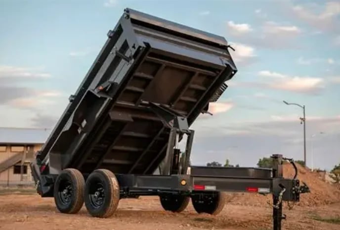 Black dump truck with raised bed on dirt lot, dual rear wheels, with cloudy sky in background