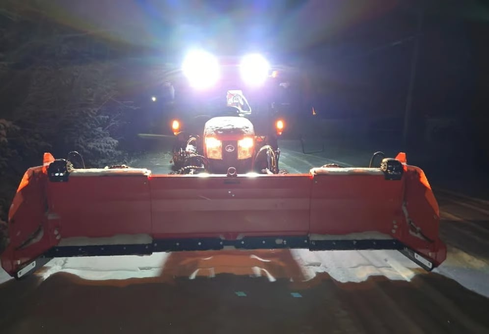 Red snow plow truck with bright headlights clearing a snowy road at night