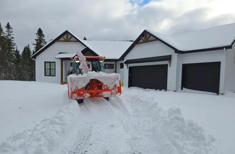 Red snow plow clearing driveway in front of modern white house with two-car garage in winter